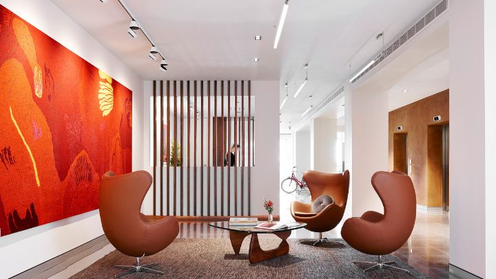 A white room with a large orange painting on the left wall and three lounge chairs in the centre